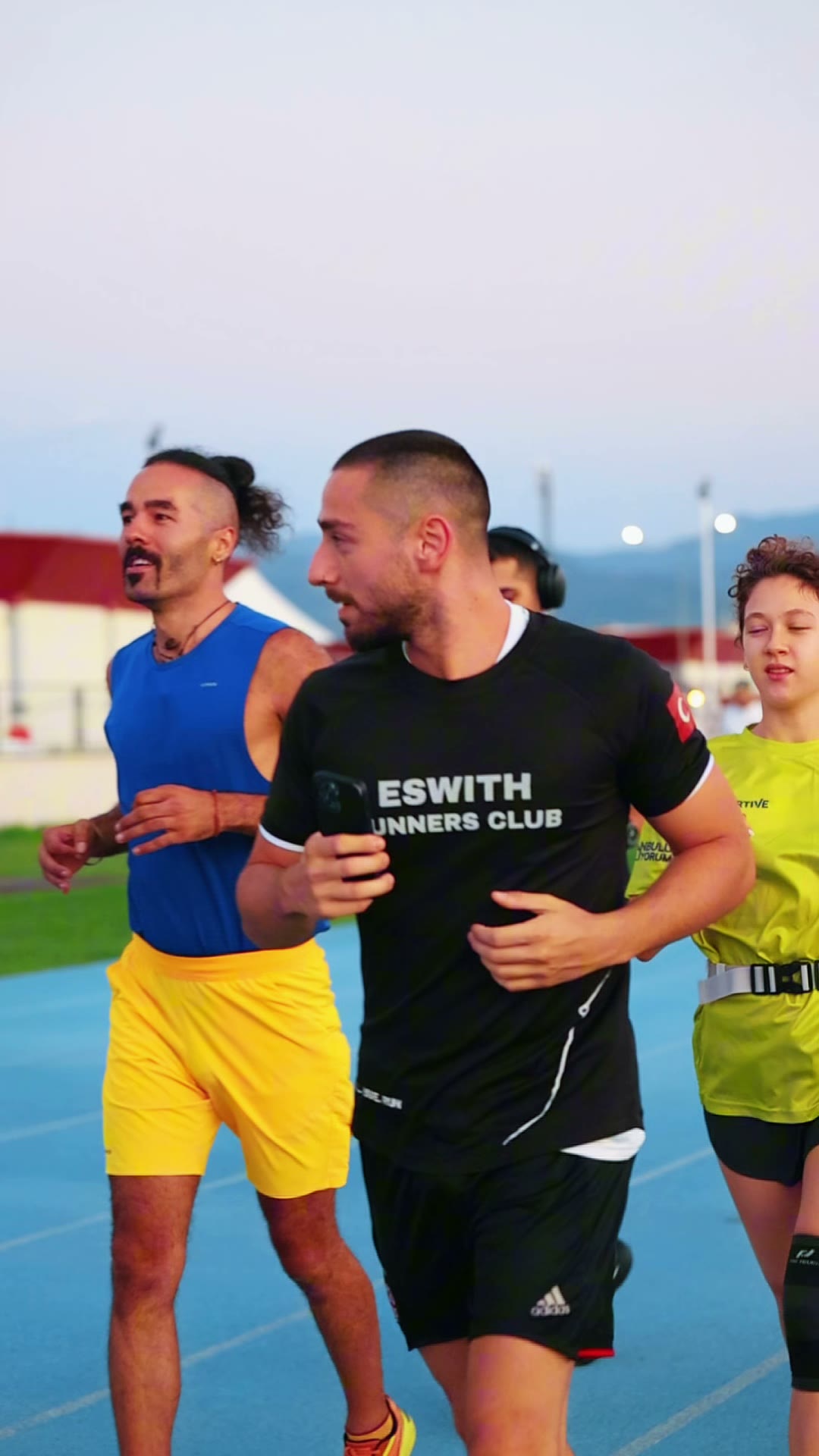 Eswith Runners Club tişörtü giyen koşucular pistte yan yana koşuyor